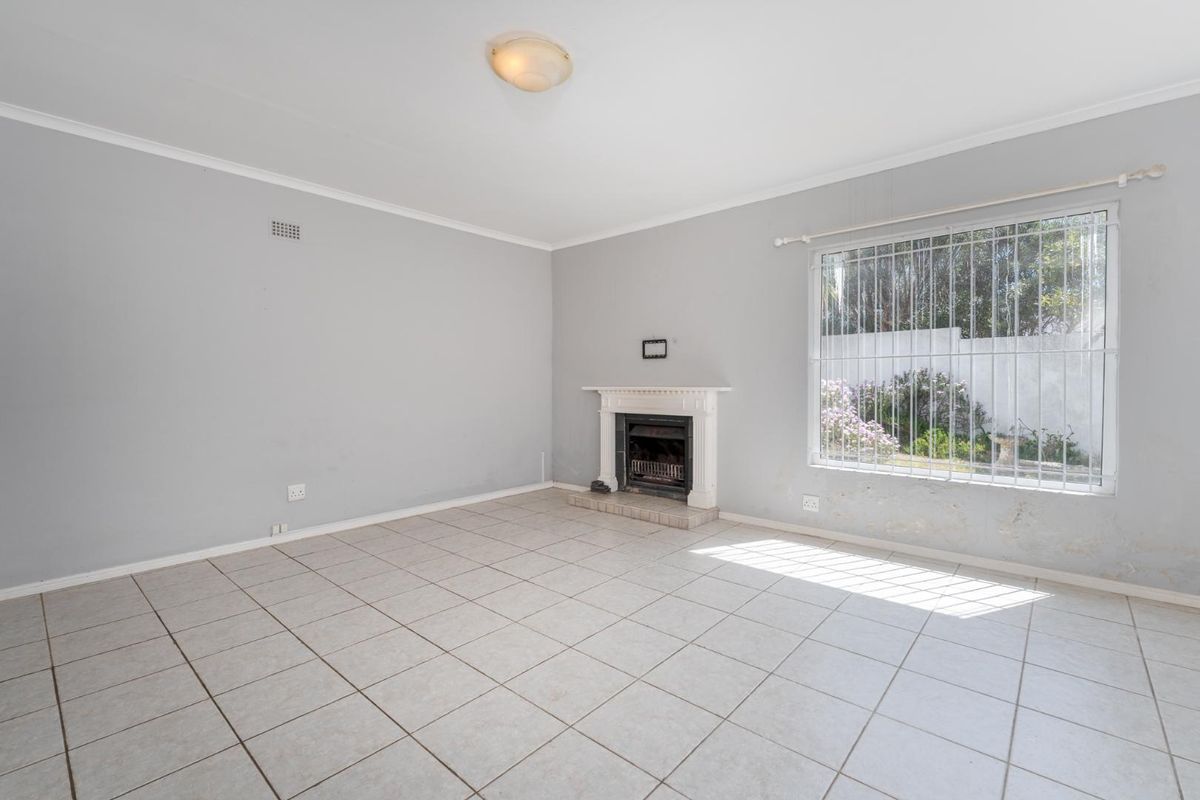 An empty living room featuring tiled flooring, a built-in fireplace, and a large window with security bars, requiring minor cosmetic repairs.