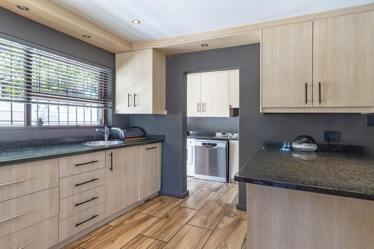 Modern kitchen featuring light wood cabinetry, dark granite countertops, wood-look tile flooring, and a convenient adjoining scullery area with additional storage and appliances.