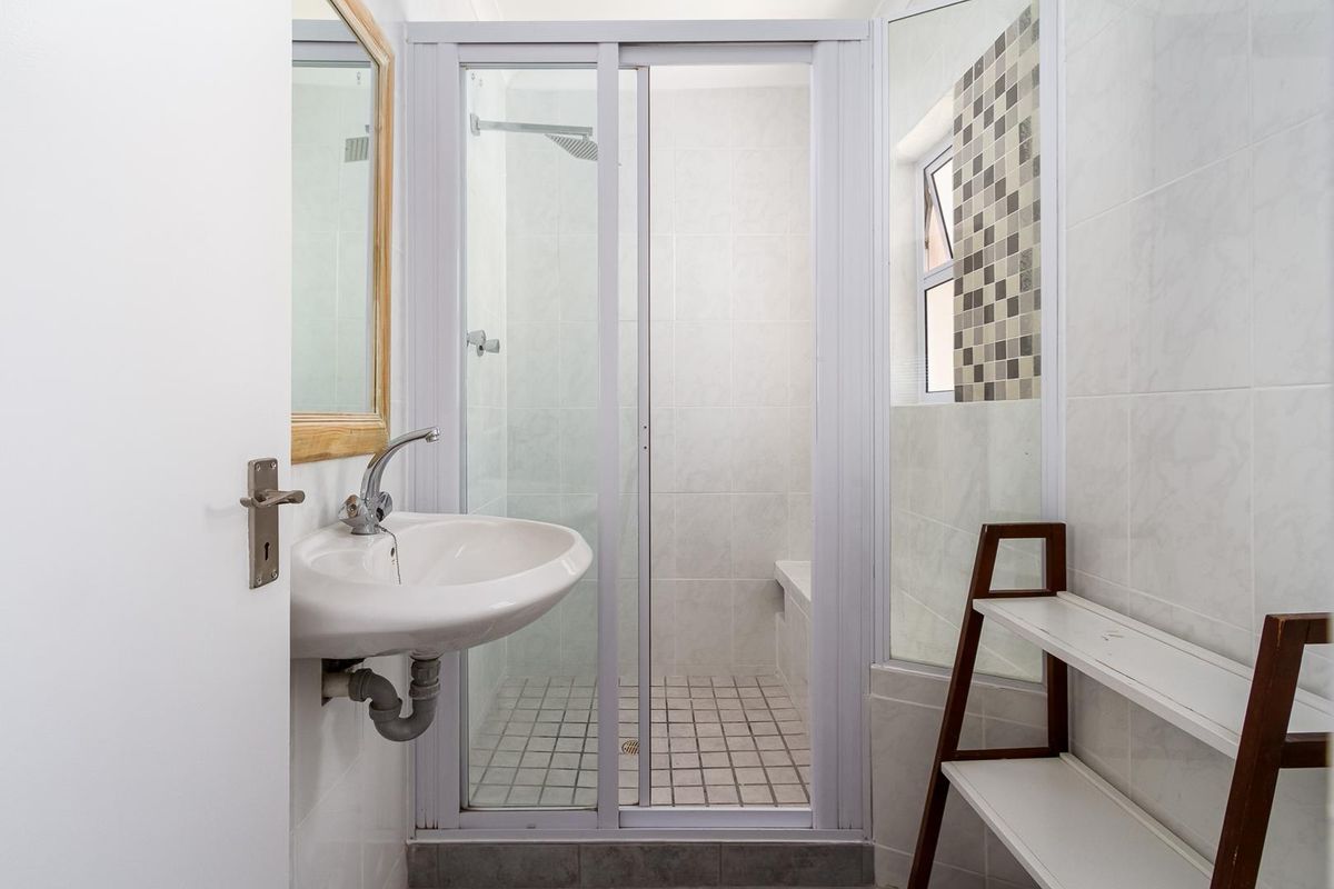 A functional bathroom featuring a wall-mounted basin, a tiled shower enclosure with a sliding door, and neutral wall tiling.
