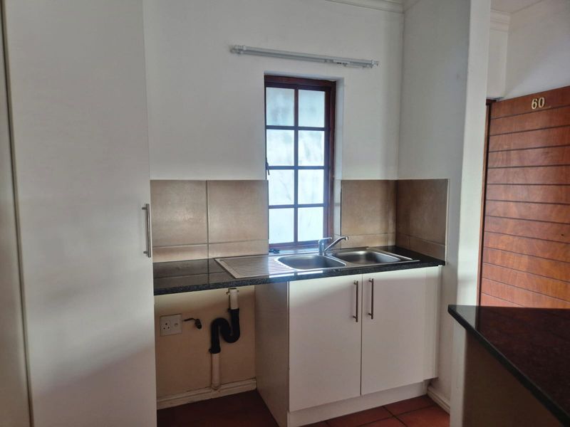 A compact kitchen area featuring a double sink, granite countertops, and built-in white cabinetry with a tiled backsplash.