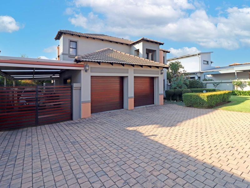 Front view of the property featuring a paved driveway, double garage with wooden doors, and an attached carport with a landscaped garden.