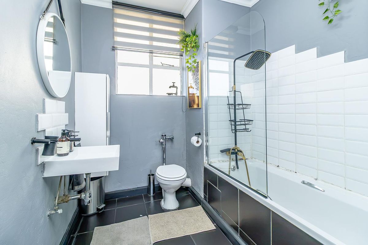 A compact bathroom featuring a wall-mounted basin, toilet, and a bathtub with a glass shower screen and modern shower fixtures.