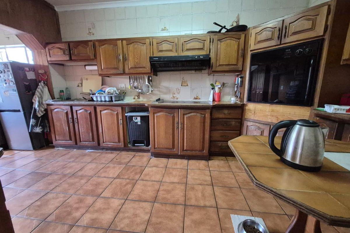 A dated kitchen featuring traditional wooden cabinetry, tiled splashbacks, built-in oven, and ceramic floor tiles, offering potential for a modern renovation.