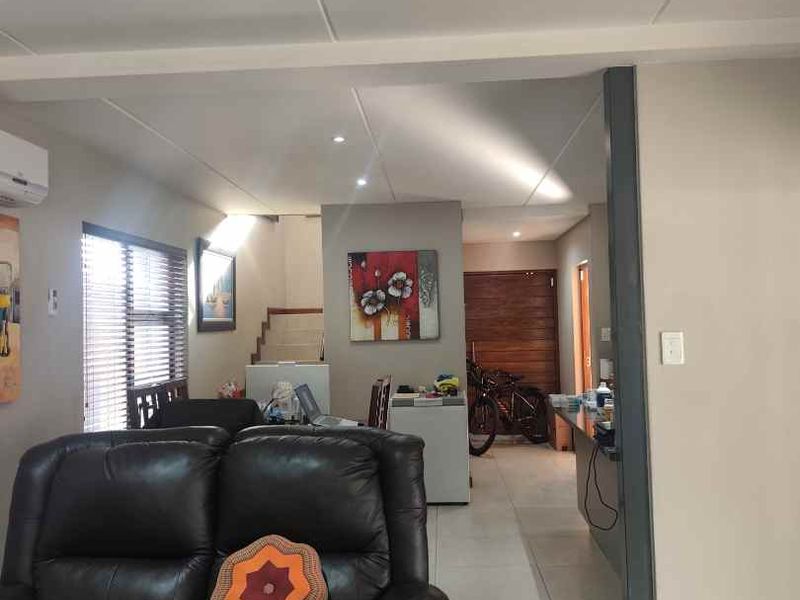 Open plan living area featuring tiled flooring, recessed ceiling lighting, and a split-system air conditioner, with a view towards the staircase and hallway.