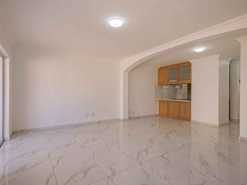 Spacious open-plan living area featuring polished marble-look floor tiles, recessed lighting, and a compact built-in kitchen nook with wooden cabinetry.