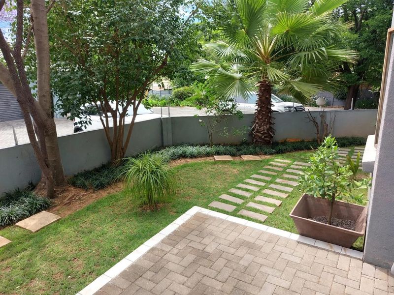 A well-maintained private garden featuring a paved patio area, stone walkway, and established perimeter walling.