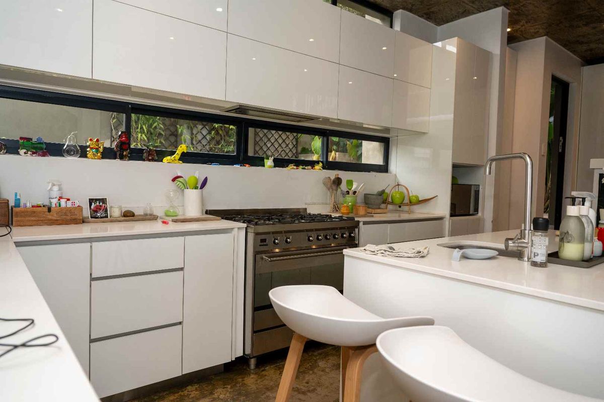 Modern kitchen featuring high-gloss white cabinetry, stone countertops, a stainless steel gas range, and a central island with a sink.