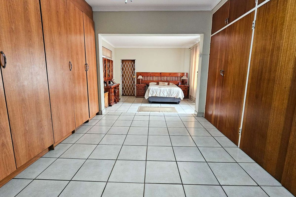 Spacious bedroom featuring extensive built-in wooden cabinetry, tiled flooring, and a secondary sleeping area accessible through a wide opening.