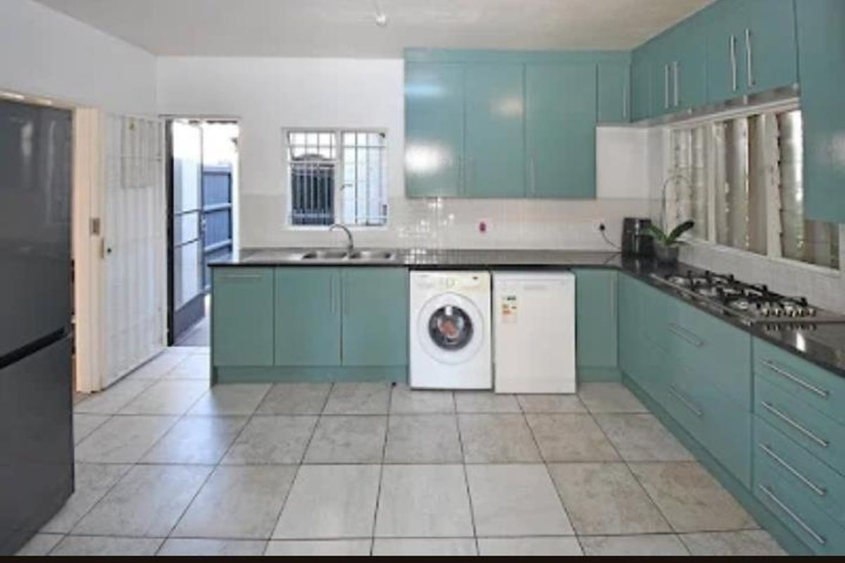 A functional kitchen featuring teal cabinetry, dark stone countertops, a built-in gas hob, and integrated laundry appliance connections.