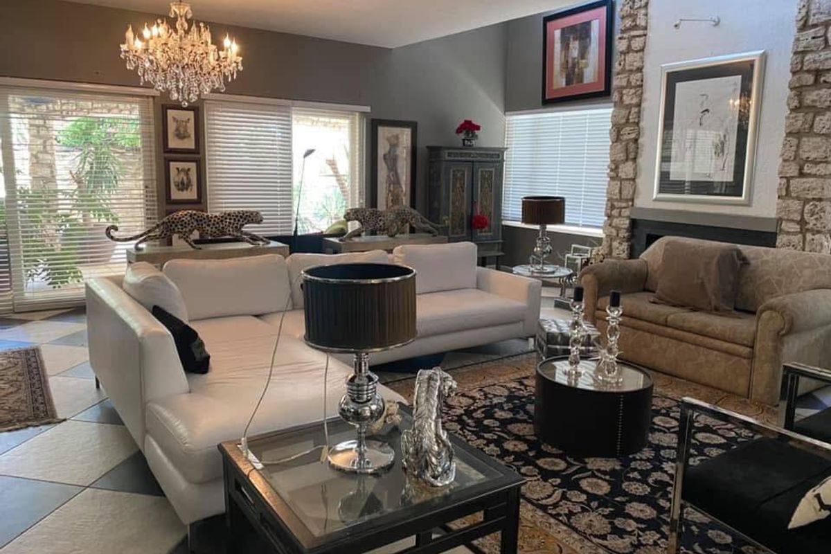 Spacious living room featuring a prominent stone-clad fireplace, large windows with blinds, tiled flooring, and an elegant crystal chandelier.