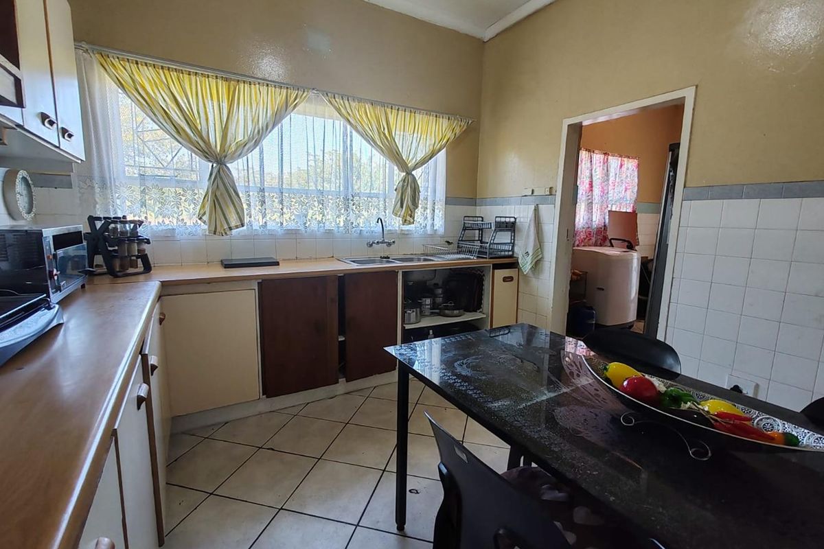 A dated kitchen featuring built-in cabinetry, tiled splashbacks, and a double sink, with an adjacent scullery area visible through the doorway.