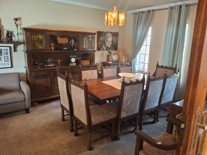 A traditional dining room featuring a large wooden dining set, carpeted flooring, and window treatments.