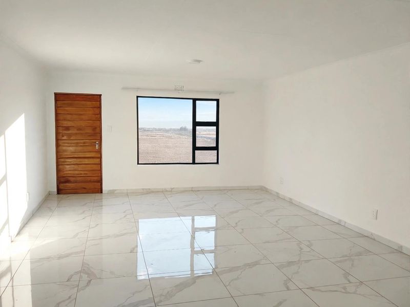A bright, empty living room featuring polished marble-look floor tiles, a wooden door, and a large window with views of the surrounding landscape.