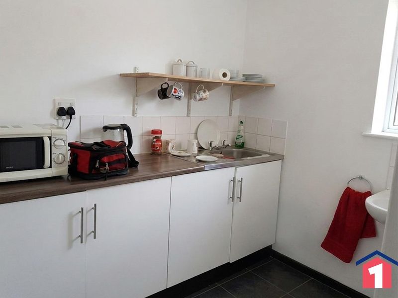 A compact kitchen area featuring white cabinetry, a stainless steel sink, tiled splashback, and practical wall-mounted shelving for storage.