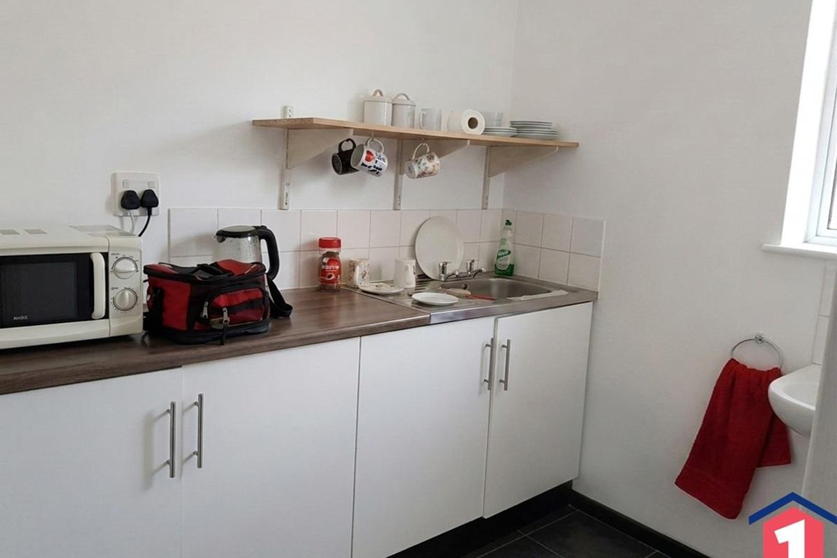 A compact kitchen area featuring white cabinetry, a stainless steel sink, tiled splashback, and practical wall-mounted shelving for storage.
