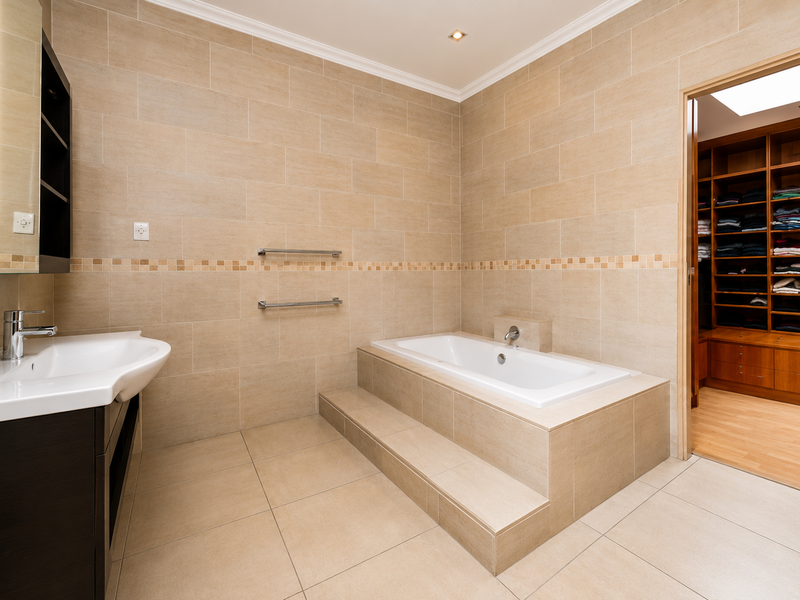 A spacious, well-maintained bathroom featuring a built-in bathtub, modern vanity, and neutral tiling, with direct access to a large walk-in closet.