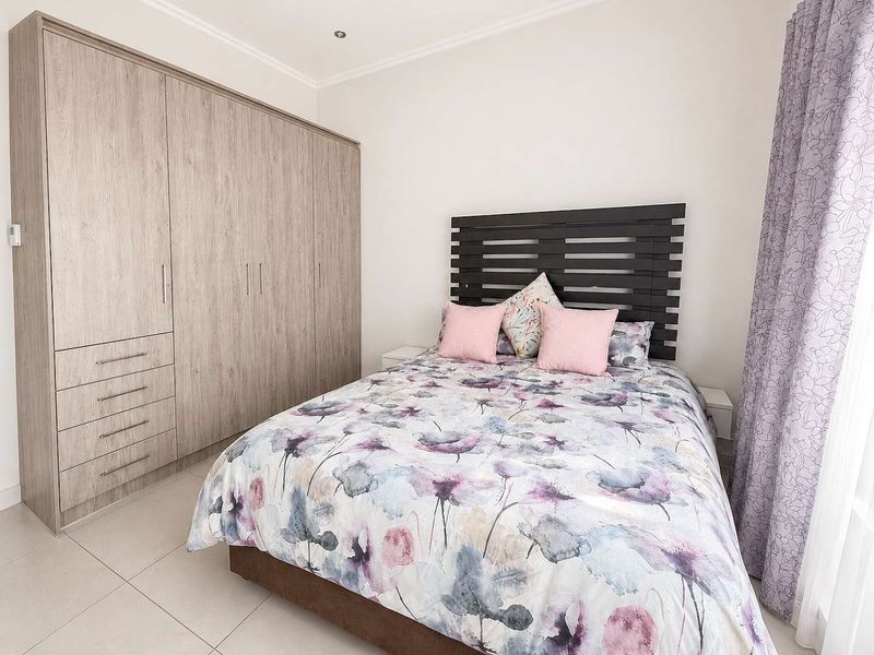 A well-maintained bedroom featuring neutral tiled flooring, recessed ceiling lighting, and a large, modern built-in wardrobe with ample storage space.