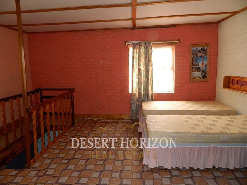 A bedroom featuring exposed beam ceilings, tiled flooring, and a wooden balustrade overlooking the lower level.