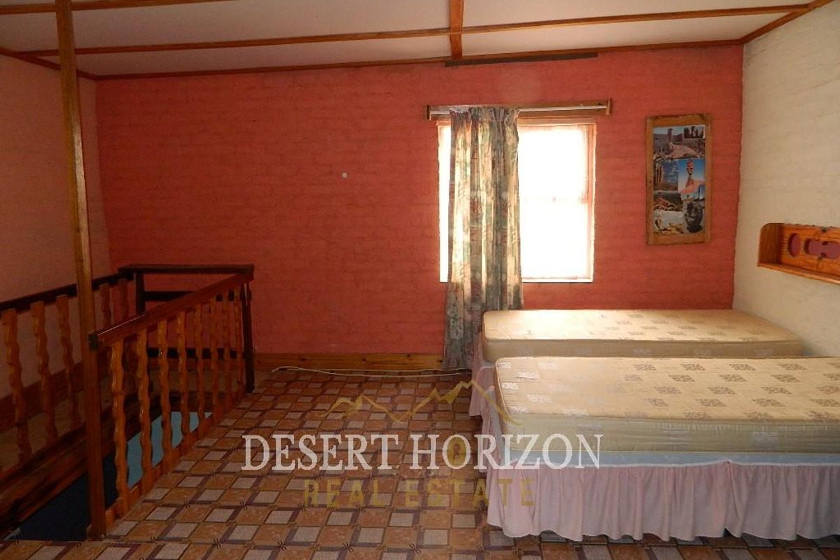A bedroom featuring exposed beam ceilings, tiled flooring, and a wooden balustrade overlooking the lower level.