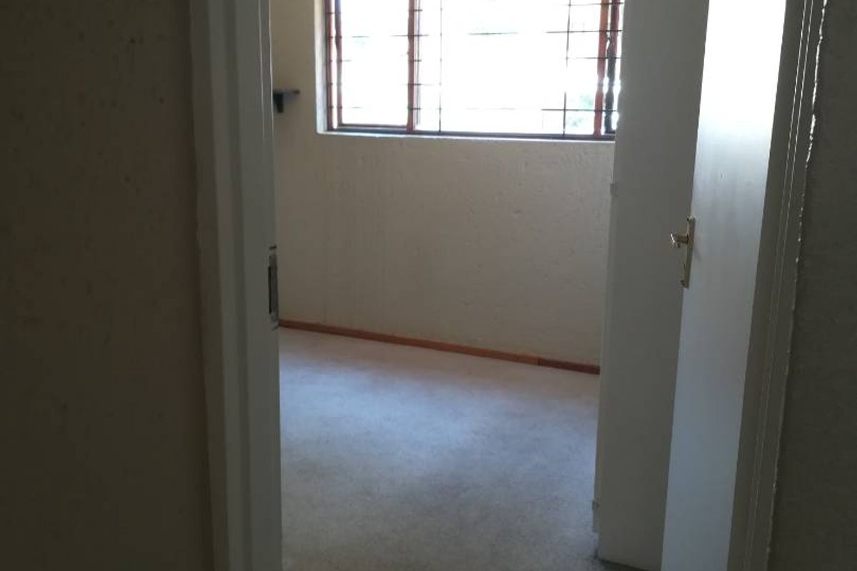 An empty bedroom featuring carpeted flooring and security bars on the window, requiring cosmetic updates to improve its overall condition.