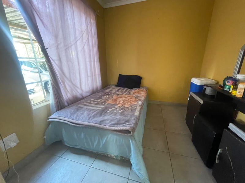 A compact bedroom featuring tiled flooring and a window with security bars, requiring cosmetic updates to the wall finishes.