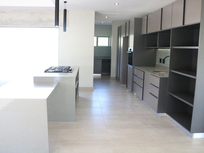 Modern kitchen featuring a large island with gas hob, sleek grey cabinetry, stone countertops, and integrated appliances in an open-plan layout.