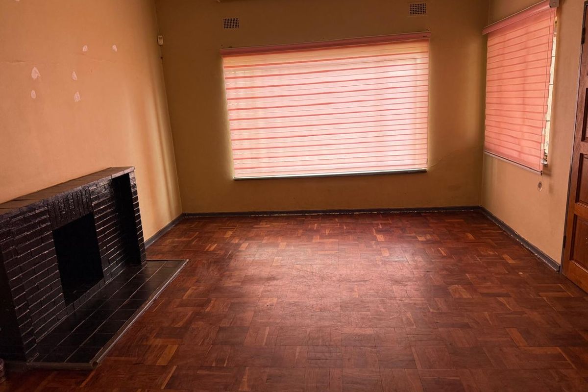 An empty living room featuring original parquet flooring and a built-in brick fireplace, offering a blank canvas for renovation.