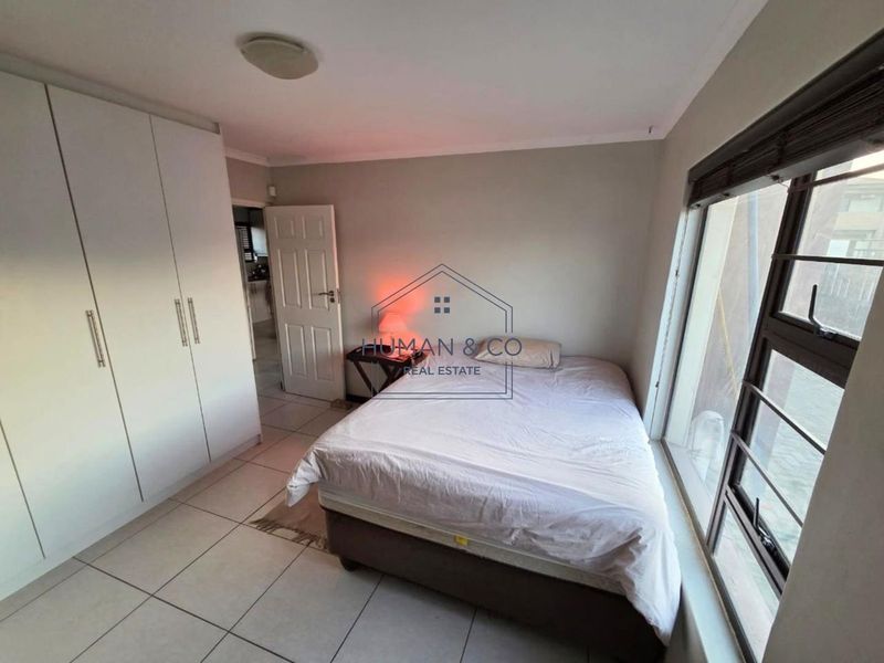 A functional bedroom featuring built-in cupboards, tiled flooring, and large aluminium-framed windows allowing for natural light.