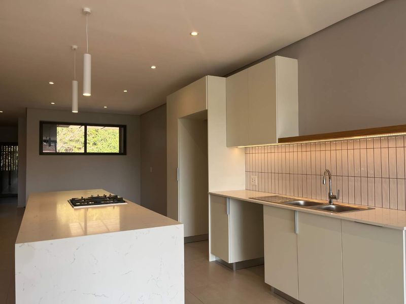 Modern kitchen featuring a large stone-topped island with integrated gas hob, sleek cabinetry, double sink, and stylish tiled backsplash with under-cabinet lighting.