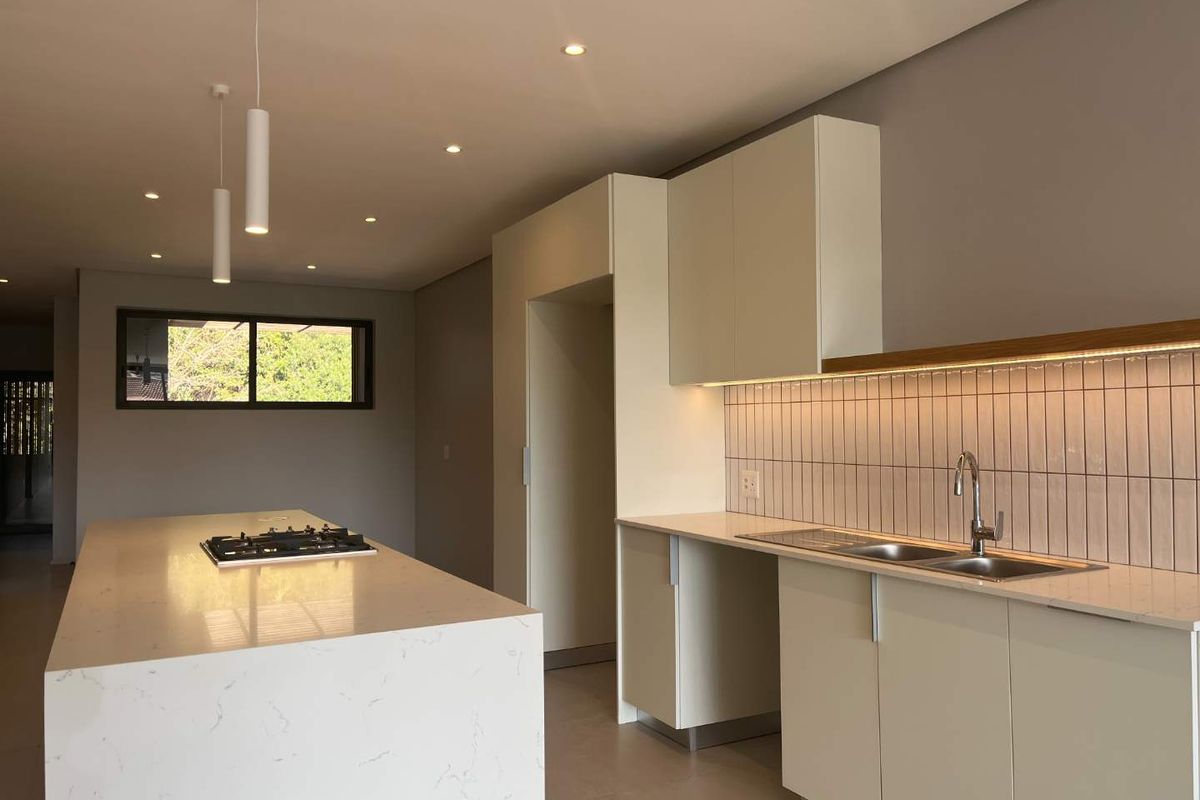 Modern kitchen featuring a large stone-topped island with integrated gas hob, sleek cabinetry, double sink, and stylish tiled backsplash with under-cabinet lighting.