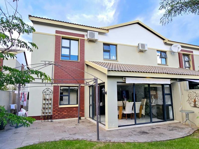 Rear view of a two-story townhouse featuring a paved patio area, sliding glass doors, and established garden space.