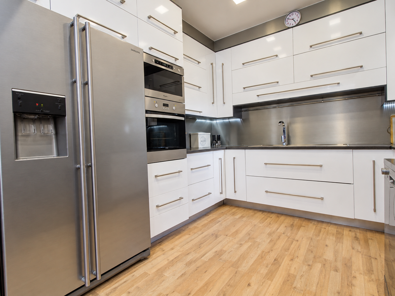 Modern kitchen featuring high-gloss white cabinetry, stainless steel appliances, integrated oven and microwave, and durable wood-look flooring with sleek metallic finishes.