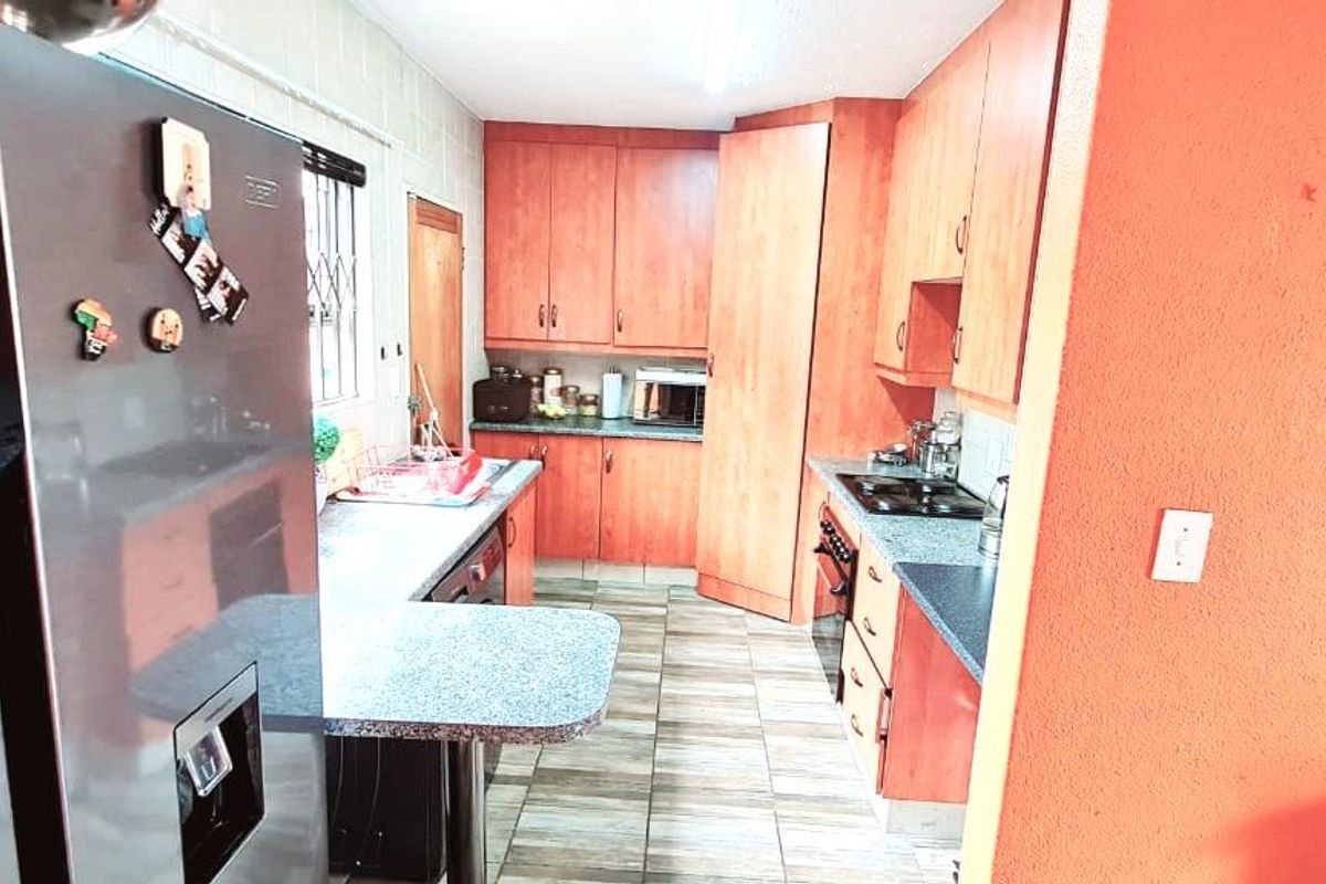 A functional kitchen featuring wood-finish cabinetry, laminate countertops, and tiled flooring, offering a practical layout for daily meal preparation.