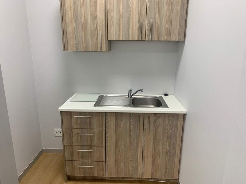 A compact office kitchenette featuring wood-grain cabinetry, a stainless steel sink, and a clean laminate countertop.