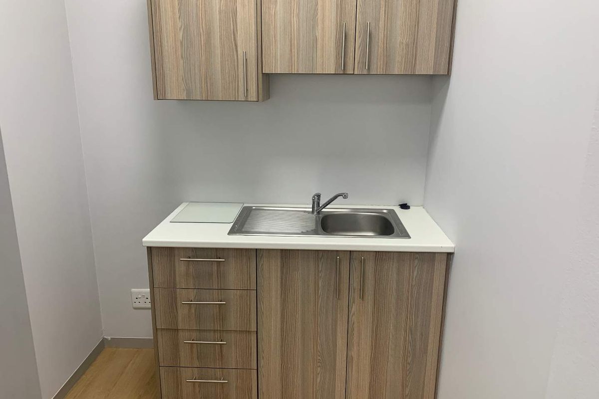A compact office kitchenette featuring wood-grain cabinetry, a stainless steel sink, and a clean laminate countertop.