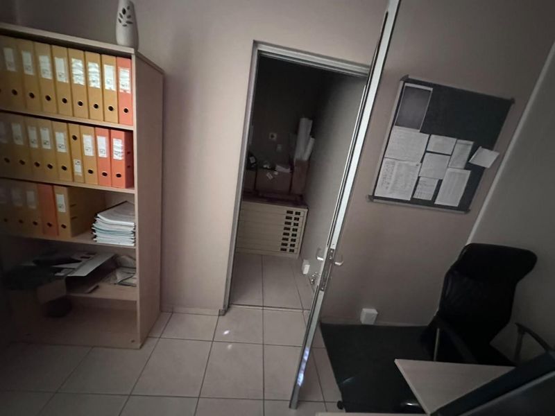 A functional office space featuring tiled flooring, a built-in storage unit, and a pin board, with an adjacent utility or storage room visible.