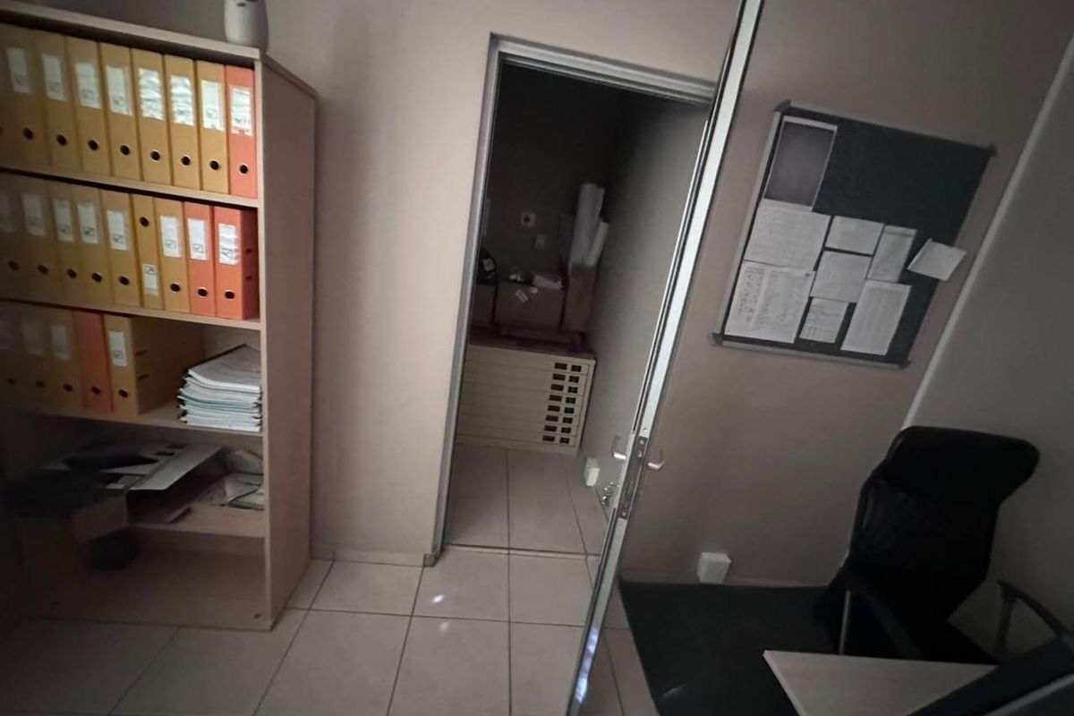 A functional office space featuring tiled flooring, a built-in storage unit, and a pin board, with an adjacent utility or storage room visible.