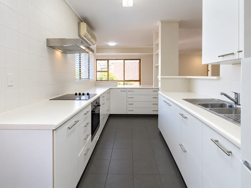 A clean, modern kitchen featuring white cabinetry, dark tiled flooring, built-in appliances, and a functional layout with ample counter space.