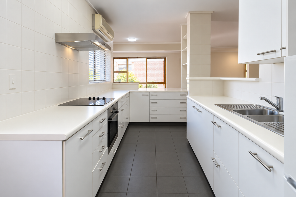 A clean, modern kitchen featuring white cabinetry, dark tiled flooring, built-in appliances, and a functional layout with ample counter space.