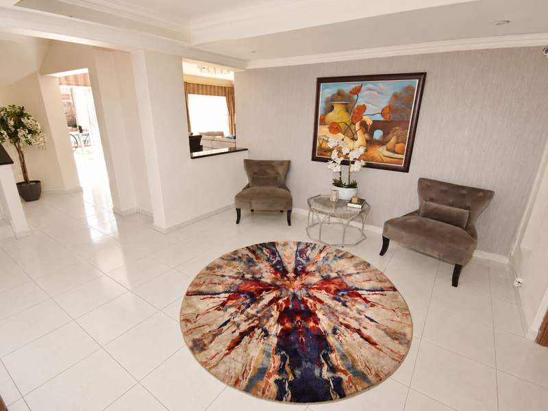 Bright and spacious entrance hall featuring polished tiled flooring, a staircase, and a pass-through window connecting to the adjacent living area.