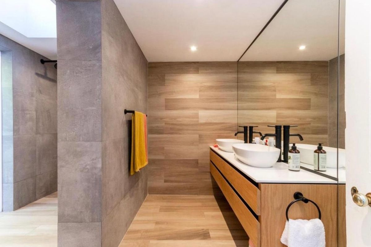 Modern bathroom featuring a double vanity with vessel sinks, wall-mounted faucets, a large mirror, and a spacious walk-in shower with contemporary tiling.
