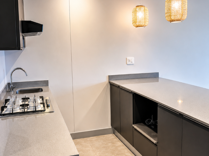 Modern kitchen featuring dark cabinetry, light quartz countertops, gas hob, integrated extractor, and stylish pendant lighting in a clean, minimalist space.