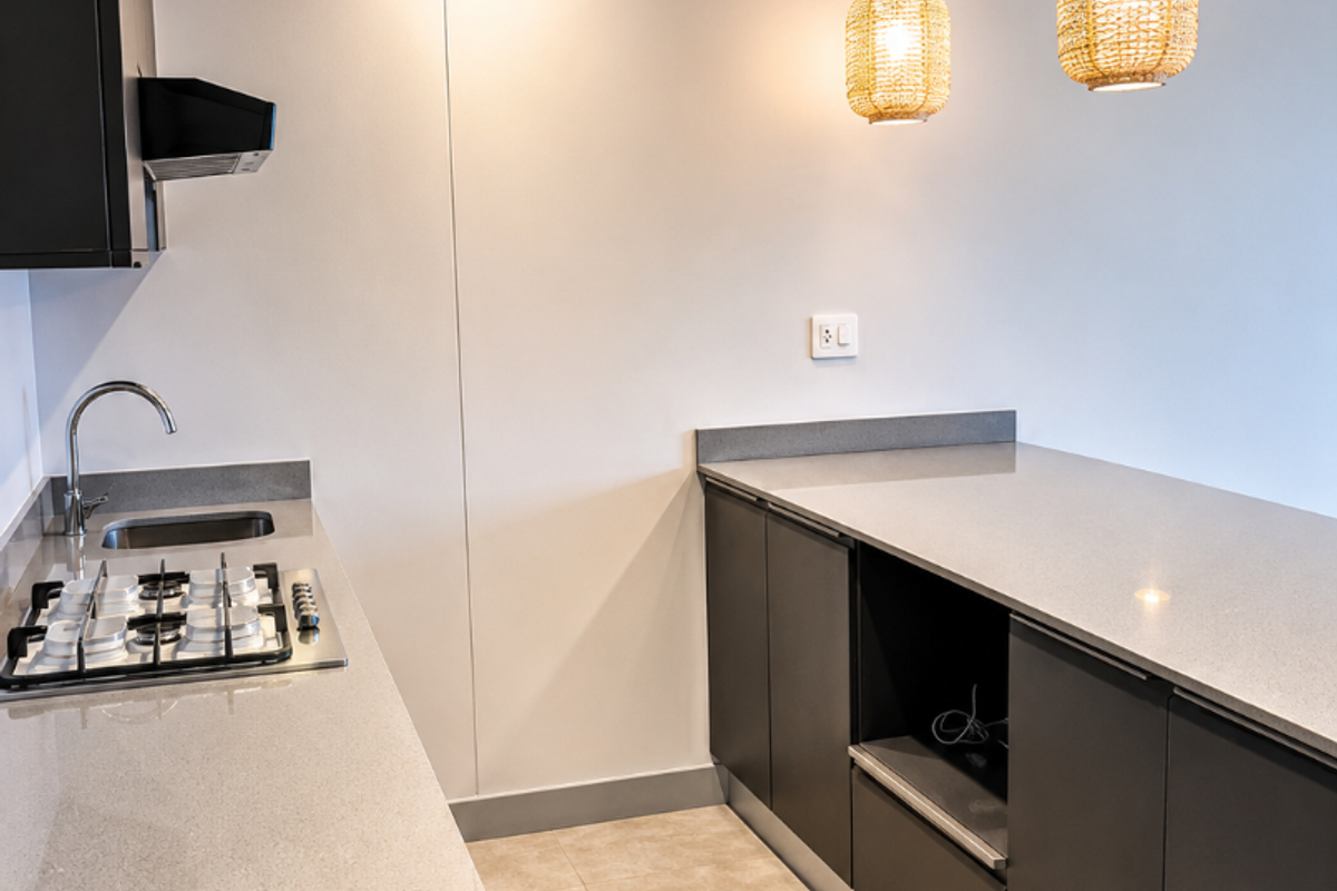 Modern kitchen featuring dark cabinetry, light quartz countertops, gas hob, integrated extractor, and stylish pendant lighting in a clean, minimalist space.
