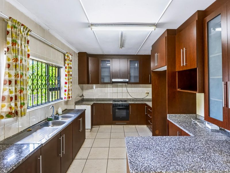 A functional kitchen featuring dark wood cabinetry, granite countertops, a built-in oven with gas hob, and tiled flooring throughout.
