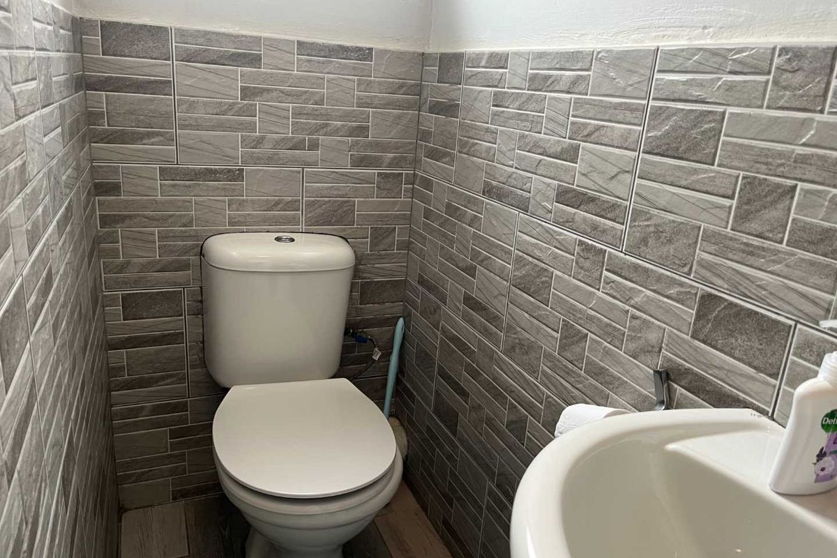 A compact bathroom featuring modern grey textured wall tiles, a white toilet, and a pedestal washbasin.