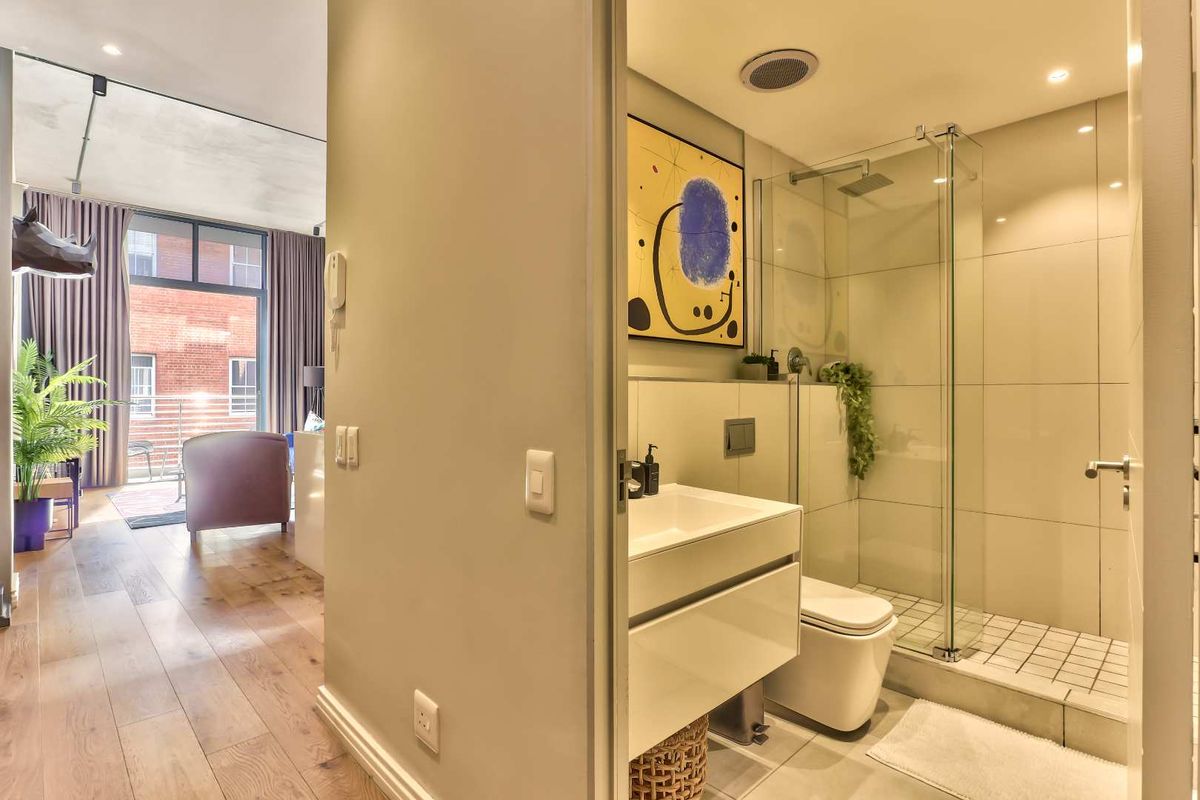 Modern bathroom featuring a walk-in shower with glass screen, wall-mounted vanity, and wall-hung toilet, adjacent to an open-plan living area.