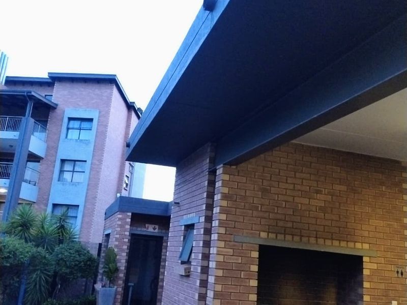 An outdoor entertainment area featuring a built-in brick braai, paved flooring, and a covered patio structure adjacent to the apartment building.