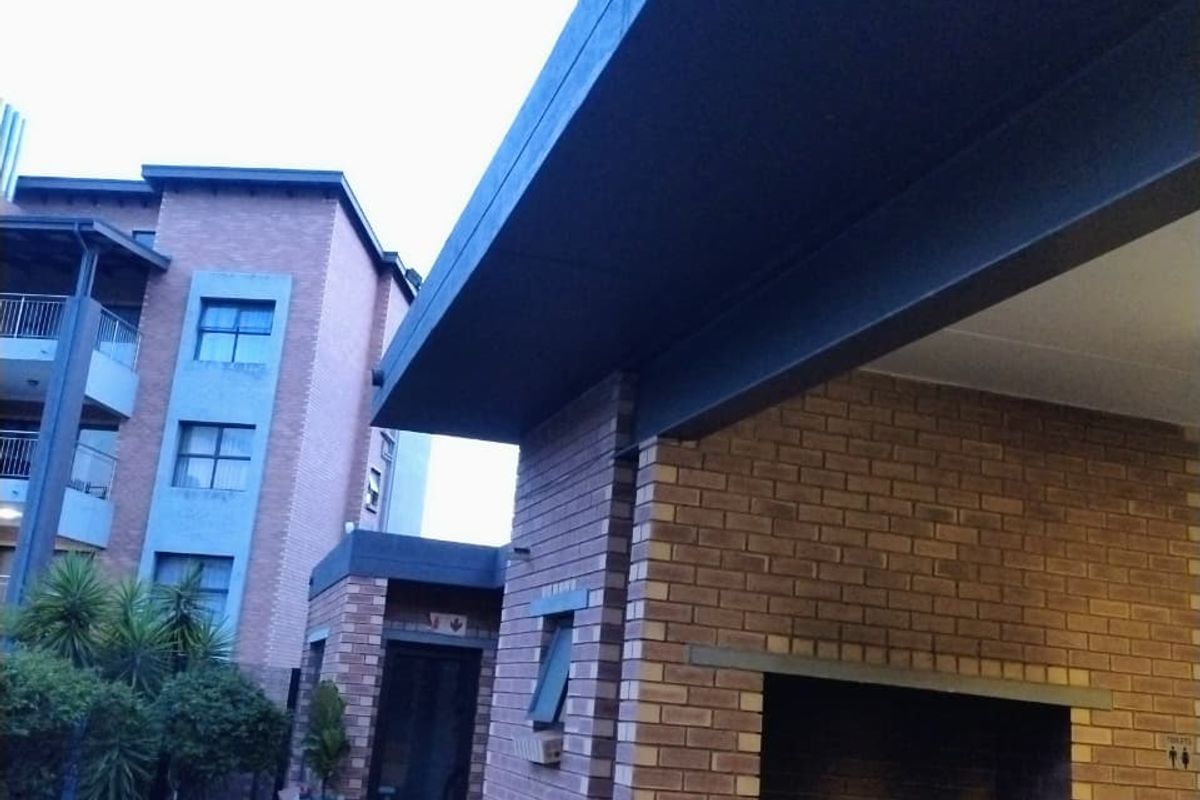 An outdoor entertainment area featuring a built-in brick braai, paved flooring, and a covered patio structure adjacent to the apartment building.