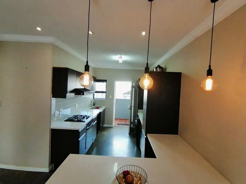 Modern kitchen featuring dark cabinetry, stone countertops, gas hob, extractor fan, and stylish pendant lighting, leading to an exterior doorway.