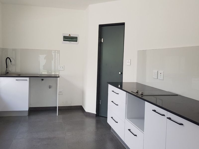 A modern, clean kitchen featuring white cabinetry, dark stone countertops, integrated hob, and a glass splashback in a bright, minimalist space.